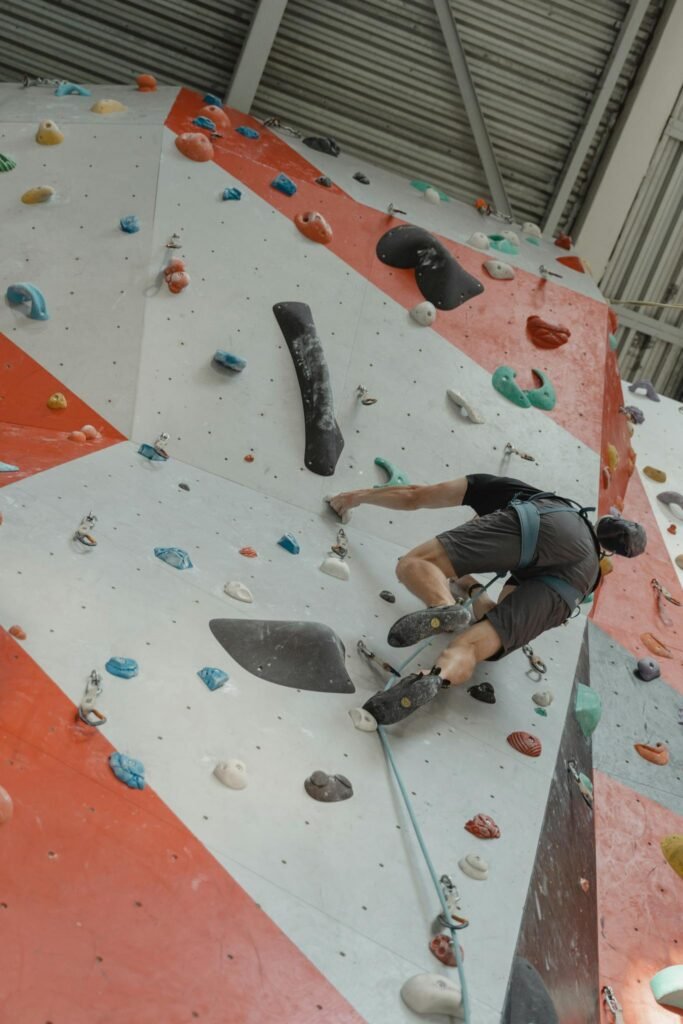 A climber skillfully ascends an indoor climbing wall using colorful holds and safety gear.
