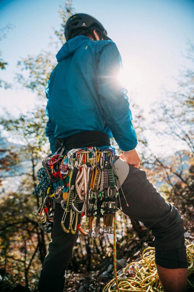 A mountain climber stands equipped with gear, facing the sun in an outdoor adventure setting.