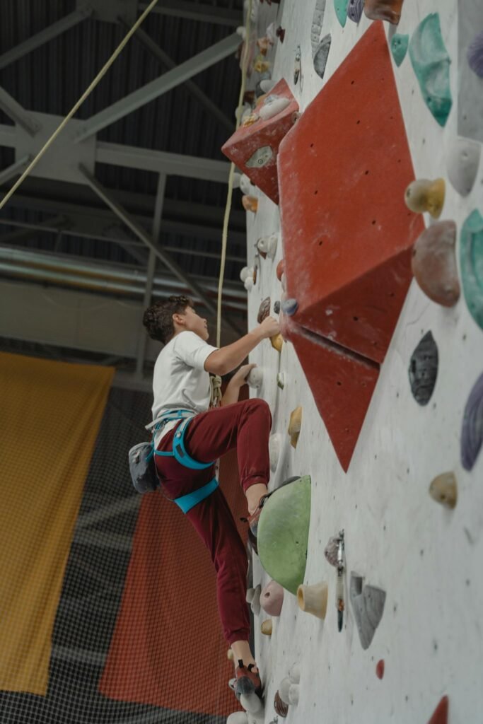 A young adult rock climber in a gym climbing a bouldering wall with harness.