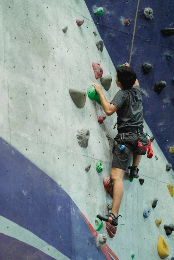 Back view of anonymous male climber with belay moving up on artificial wall during training in bouldering center