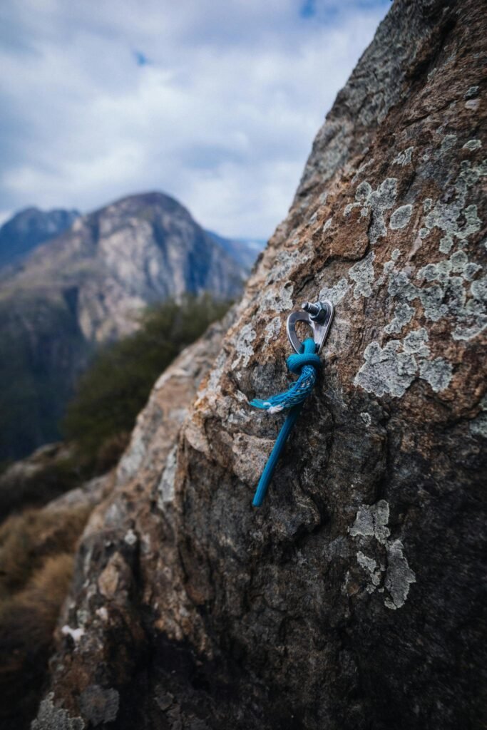 Close-up of a climbing anchor embedded in a rocky mountainside under a cloudy sky, showcasing outdoor adventure.