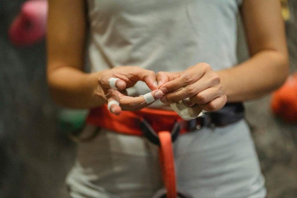 Female climber preparing for indoor climb by taping fingers, emphasizing gear and safety.